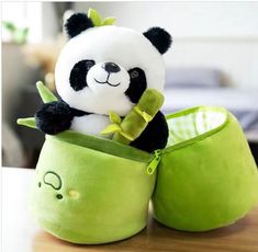 a stuffed panda bear sitting in a green pot on top of a wooden table next to a pillow