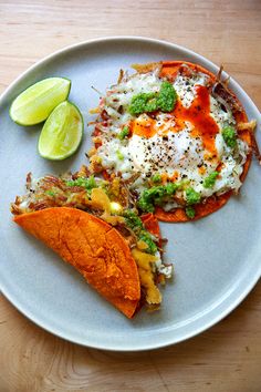 two tacos are sitting on a plate with lime wedges and an egg in the middle