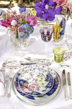 the table is set with plates, silverware and flowers in vases on it