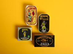 three different tins with labels on them sitting on a yellow surface next to each other