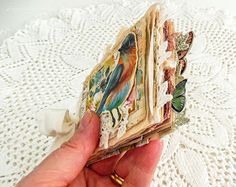 a hand holding an open book on top of a white doily covered table cloth