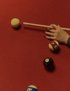 a woman's hand reaching for pool balls on a red table with cues