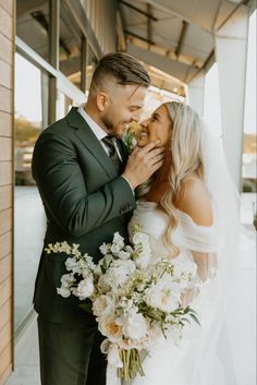 a bride and groom are posing for a wedding photo in front of a building with flowers