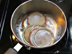 three glass jars are in a saucepan on the stove top, filled with water