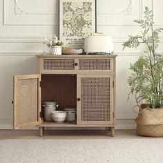 a wooden cabinet sitting next to a potted plant on top of a rug in front of a white wall