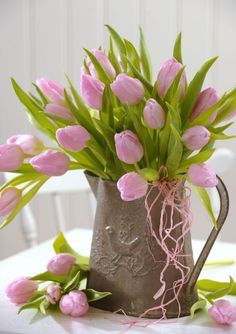 a watering can filled with pink tulips sitting on top of a white table