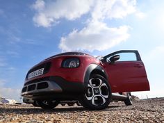 a red car parked on top of a gravel covered field next to a blue sky