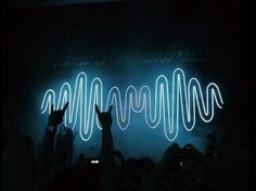 people raising their hands in the air at a concert with neon lights and sound waves