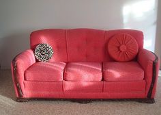 a red couch sitting in a living room next to a wall with a black and white pillow on it