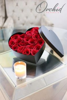 a heart shaped box filled with red roses on top of a table next to a candle