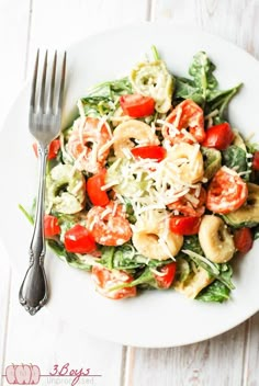 a white plate topped with pasta and veggies next to a knife and fork