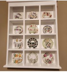 a white shelf filled with lots of different plates on top of each other in front of a wall