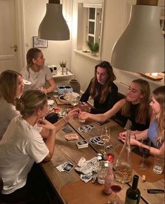 a group of women sitting around a wooden table with wine glasses on top of it