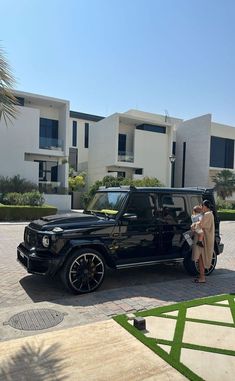 a man and woman standing next to a black car in front of some white buildings