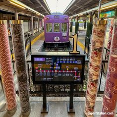 a purple train traveling through a train station next to tall pillars with writing on them