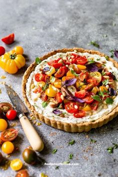 a tart with tomatoes, onions and other vegetables on it next to a knife