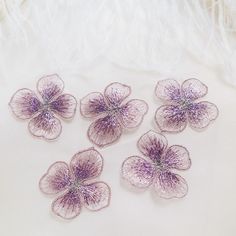 four purple flowers are on a white surface with feathers in the backgrounnd