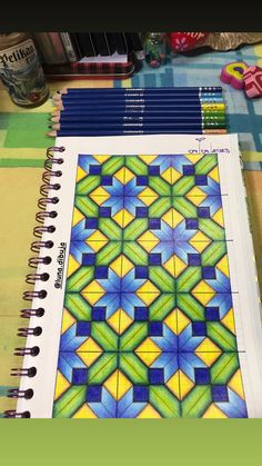 some colored pencils are sitting on top of a notebook with an artistic design in the middle