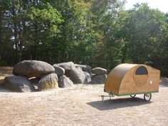 a camper trailer parked next to some large rocks and trees in the back ground