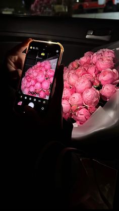 a person holding a cell phone in front of a bouquet of pink roses