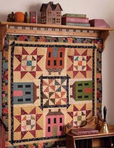 a quilt hanging on the wall next to a wooden shelf with books and other items