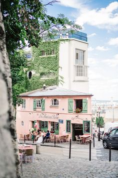 a pink building with green shutters and people sitting at tables