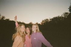 three girls are posing for the camera with their arms in the air and trees behind them