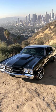 a black car parked on top of a dirt hill next to a cityscape