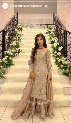 a woman standing in front of stairs wearing a long dress with an elaborate design on it