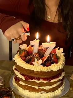 a woman sitting in front of a cake with lit candles on it and looking at the camera