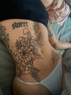 a woman laying on top of a bed with tattoos on her stomach and lower back