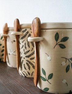 three ceramic pots with wooden spoons and leaves painted on them, lined up against a wall