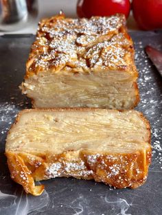 two pieces of bread with powdered sugar on top and apples in the back ground