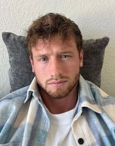 a man sitting on a couch wearing a plaid shirt and looking at the camera with a serious look on his face