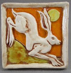 a ceramic tile with a white rabbit on it's back and an orange background