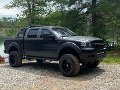 a black truck parked on top of a gravel road next to a body of water