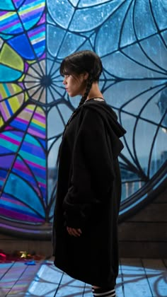 a woman standing in front of a colorful stained glass window with her back turned to the camera