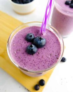 two glasses filled with blueberry smoothie on top of a cutting board