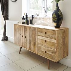 a wooden cabinet with wine bottles and vases on it in front of a window