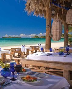 an outdoor dining area on the beach with tables and chairs set up for two people