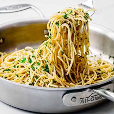 spaghetti being cooked in a pan with tongs