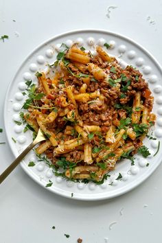 a white plate topped with pasta covered in sauce and parsley next to a spoon