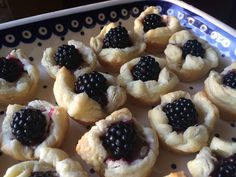 small pastries with blackberries on them in a blue and white tray