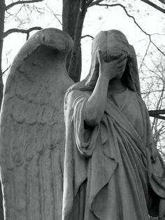 an angel statue is holding his head to his hand while standing next to a tree