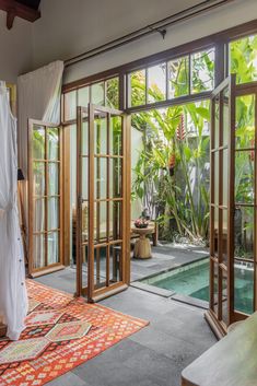 a bedroom with an open door leading to a pool and lush vegetation in the background