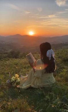 a woman sitting on top of a lush green field holding a book in her hands