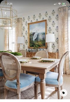 a dining room table with blue chairs and a bird painting on the wall behind it