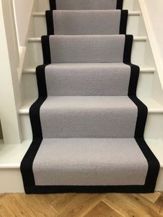 carpeted stairs with black trim and white handrails on the bottom, leading up to