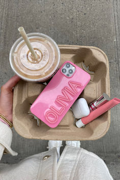 a person holding a cup and cell phone in a tray with personal items on it