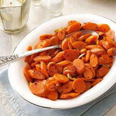 a white bowl filled with cooked carrots on top of a blue cloth next to a silver spoon